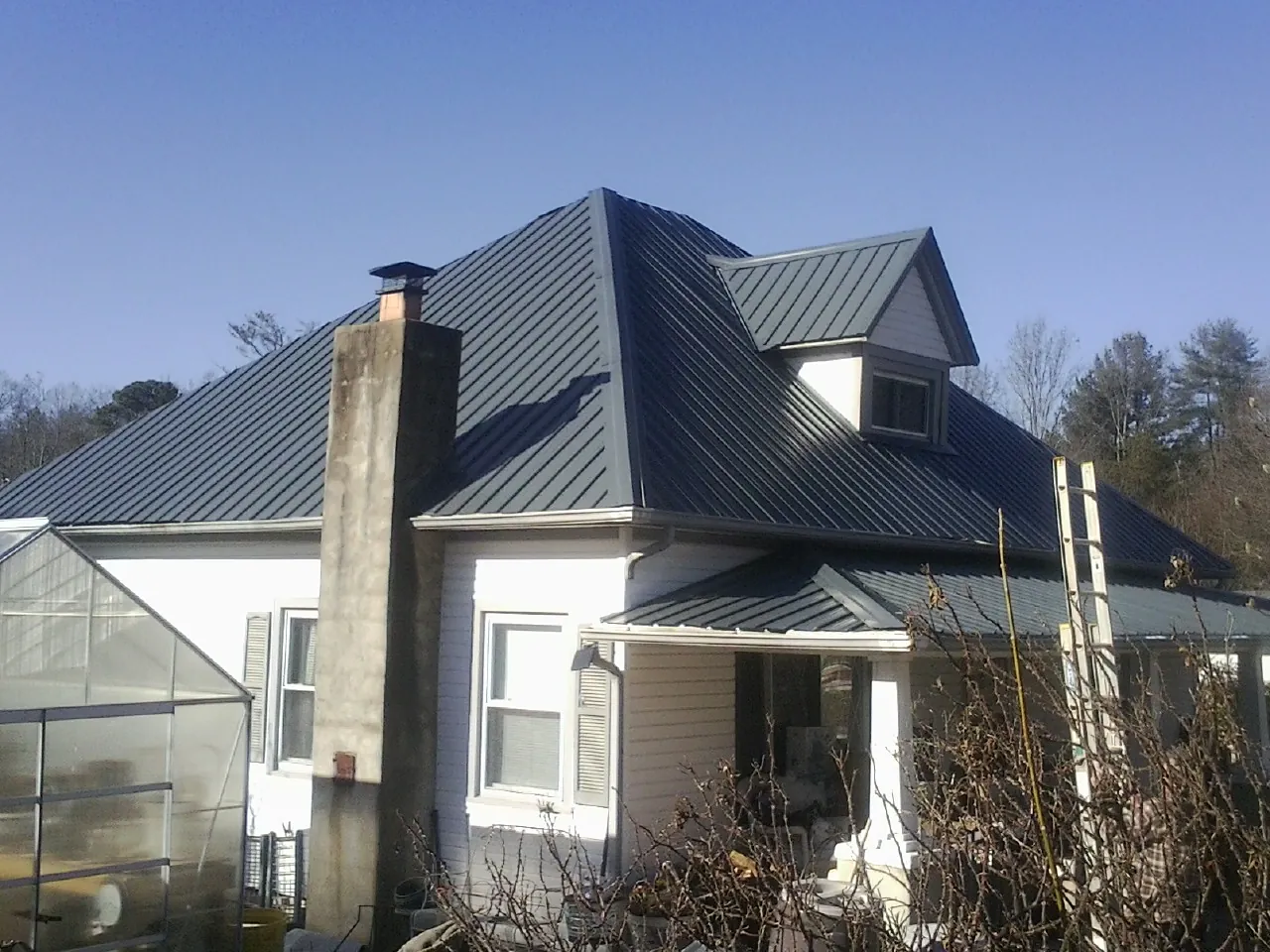 Dark blue standing seam metal roof on a white farmhouse with dormer — Slate & Tile Roof Repair by Roofing Brothers in Lennon