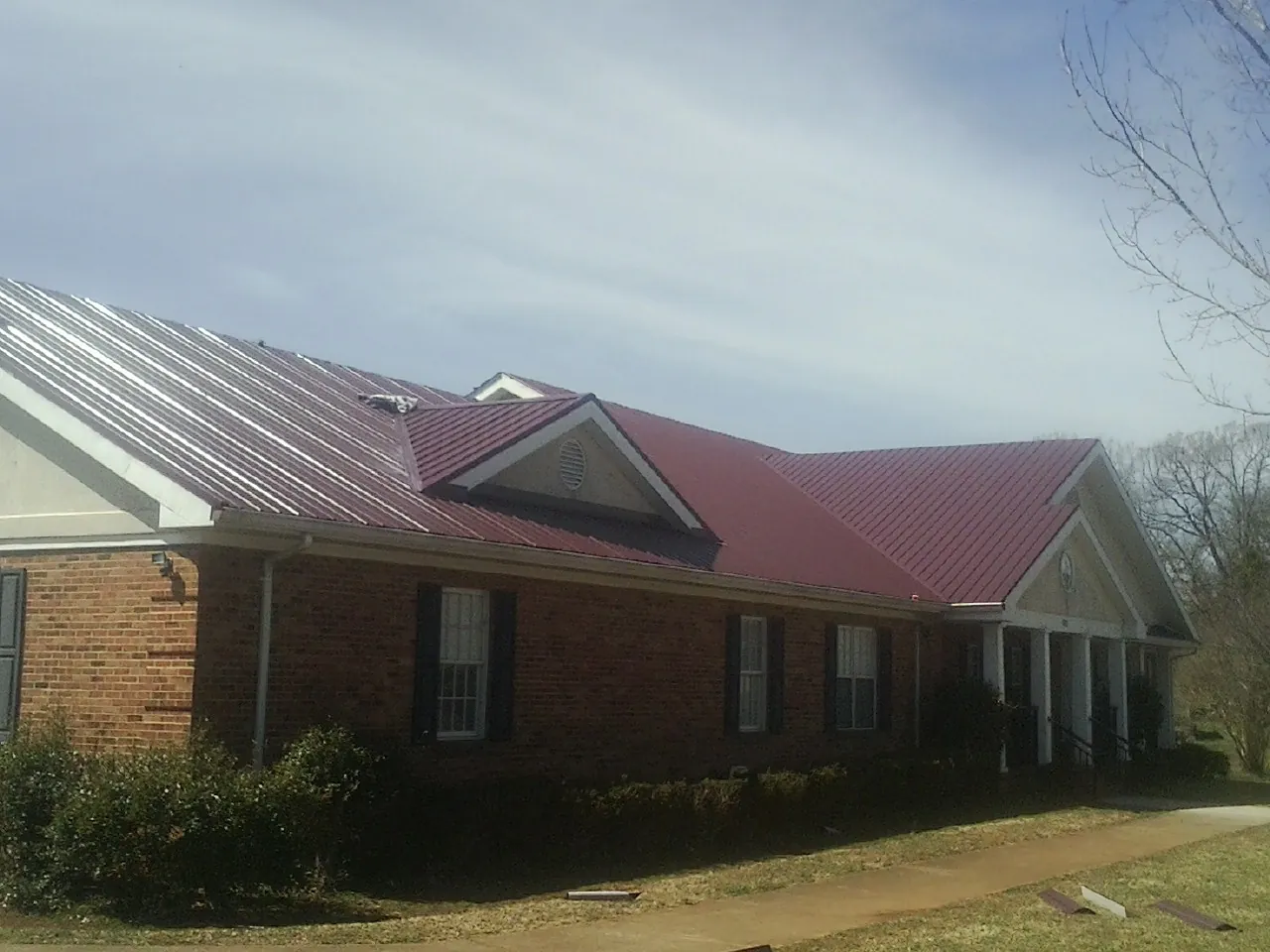 Red metal roof with gabled entries on a long brick building, from a Hail Damage Roof Repair job in Lennon