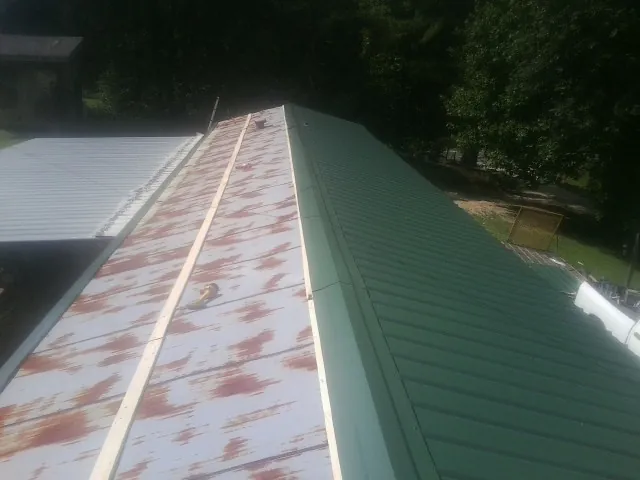 Old rusted panels beside newly installed green metal roofing — Wind Damage Roof Repair by Roofing Brothers in Lennon
