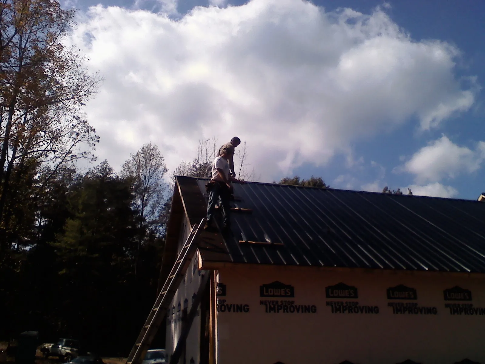 Roofer fastening dark metal panels high against a cloudy sky, from a Roof Inspection job in Lennon
