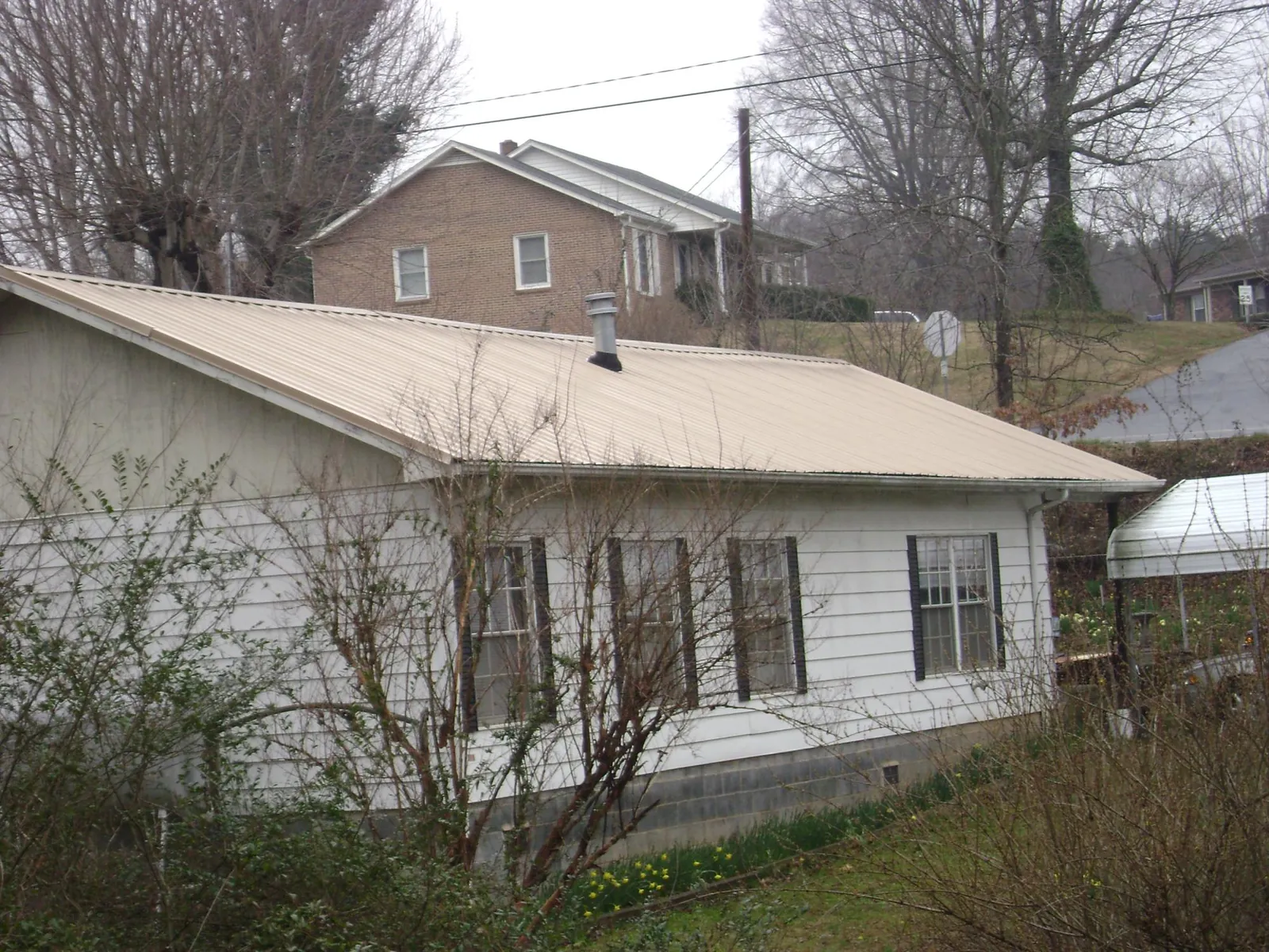 Tan metal roof on a white sided house set into a hillside — Commercial Roofing by Roofing Brothers in Lennon