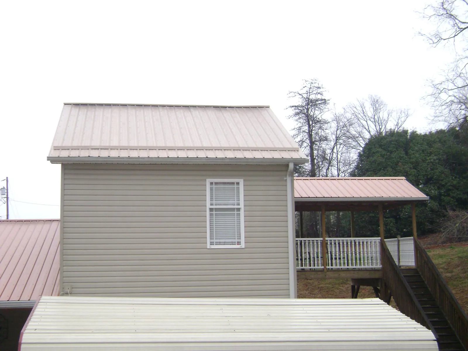Tan metal roofs on a two story addition and attached porch, from a Roof Replacement job in Lennon